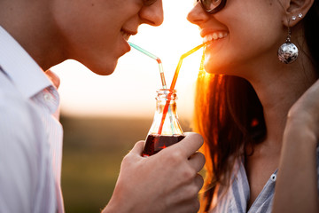 Beautiful dark-haired girl and a young man  in sunglasses are drinking from one bottle a drink...