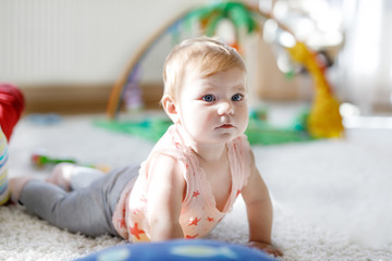 Fototapeta premium Little cute baby girl learning to crawl. Healthy child crawling in kids room with colorful toys. Back view of baby legs. Cute toddler discovering home and learning different skills