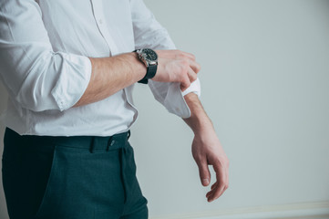 A man in a white shirt and a stylish watch in his arms rolls up his sleeves.