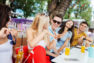 A company of good-looking friends laughing and drinking yellow cocktails and socialising at the table in the nice summer cafe. Cheers. Entertainment, having good time. Friendship.