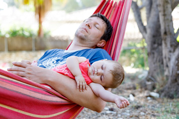Cute adorable baby girl of 6 months and her father sleeping peaceful in hammock in outdoor garden. Closeup of beautiful child, little newborn kid sleeping. Tired dad, man in bed with daughter