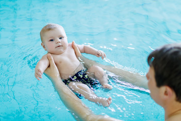 Fototapeta na wymiar Happy middle-aged father swimming with cute adorable baby in swimming pool. Smiling dad and little child, newborn girl having fun together. Active family spending leisure and time in spa hotel