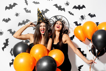 Two charming young women in witches hats are with black and orange balloons on a white background...