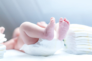 Feet of newborn baby on changing table with diapers. Cute little girl or boy two weeks old. Dry and healthy body and skin concept. Baby nursery.