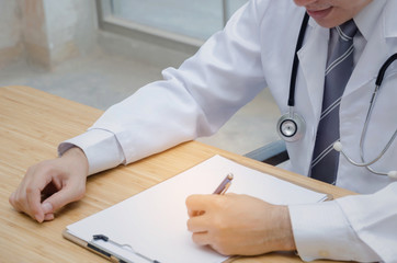 doctor or pharmacist with stethoscope on neck working with laptop computer and writing on paperwork at worktable in hospital or clinic, medical technology, disease treatment and health care concept