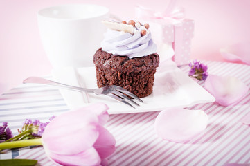 Black coffee and chocolate cupcake with icing on a pink background with tulip petals and coffee beans