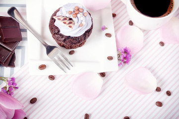 Black coffee and chocolate cupcake with icing on a pink background with tulip petals and coffee beans	