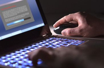 Man installing software in laptop in dark at night. Hacker loading illegal program or guy...