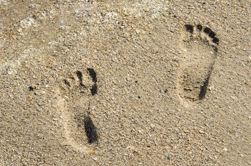 two children's footprints in the sand near the sea foam in summer
