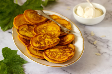 Homemade pumpkin pancakes served with sour cream on a light background.