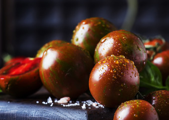 Brown cherry tomatoes with sea salt and green basil on dark table, autumn harvest, selective focus