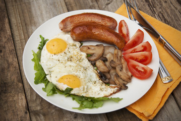 English breakfast. Eggs, sausages, mushrooms, tomatoes, toast bread. Eating tasy food over rustic wooden table. Copy space.