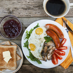 English breakfast. Eggs, sausages, mushrooms, tomatoes, toast bread. Eating tasy food over rustic wooden table. Copy space. Square image.