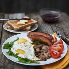 English breakfast. Eggs, sausages, mushrooms, tomatoes, toast bread. Eating tasy food over rustic wooden table. Copy space. Square image.
