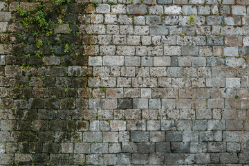 Fototapeta premium The texture of the old masonry of stone and concrete. The wall on the streets of Italy. Covered with moss and grass, ancient blocks. Historical paving and paving slabs.