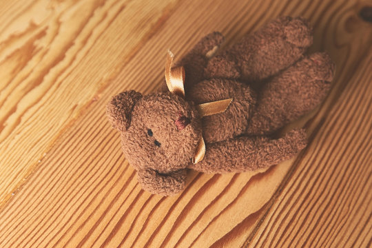 A brown teddy bear lying on a wooden surface. This image can be used to represent the concept of childhood. 