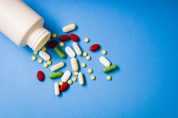 An open white bottle with spilled colorful medications