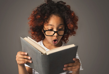 Surprised little black girl with book at gray background