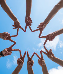 a circle of ten hands making peace signs under a blue sky with white clouds