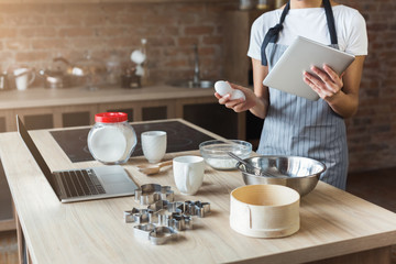 Woman baking pastry with recipe on digital tablet