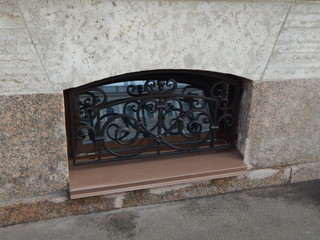 The basement window with a metal patterned lattice and the reflection of the house in front of it
