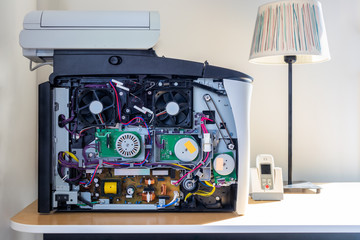 Front close up inside of a office copier machine. Electronic parts and fans. Standing on a desk with a table lamp.
