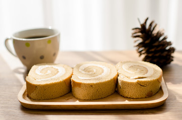 Coffee roll cake and a cup of coffee on wooden table.