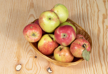 Brown basket full of ripe apples on a wooden table
