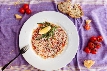 Carpaccio of salmon covered with parmesan, arugula and lemon slice. Top view
