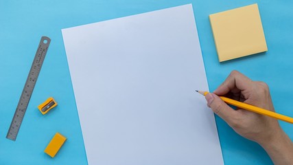 Stationery and right handed with pencil writting in white paper on blue color background, flat lay...