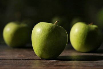 Green apples on a brown wooden table on a dark background on a sunny day