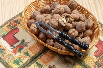 Nutcracker on top of some walnuts and a cracked walnut on a table cloth on a wooden table
