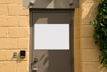 Beige metal door in yellow cinder block wall with white blank sign