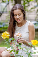 Young girl in a white dress in a summer park smelling a rose
