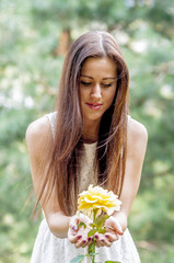 Young girl in a white dress in a summer park smelling a rose
