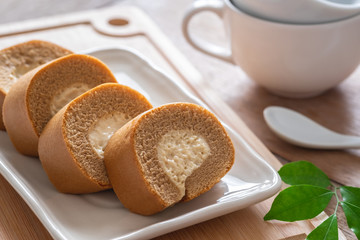 Coffee roll cake with cream on plate and coffee cup