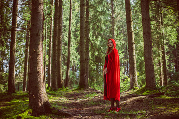 Naklejka premium Concept of Halloween. Beautiful and simple costume of little red hood. Mysterious hooded figure in misty forest. Girl in red raincoat. Cosplay Fairy Tale Little Red Riding Hood 