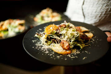 Waiter hold black plate caesar salad with chicken inside
