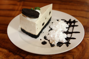 Sweet creamy cheesecake decorated by chocolate cookies on top and whip cream on white plate.