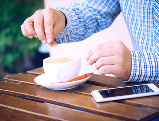 Young man hands holding sugar bag and sweetens coffee in a cafe.
