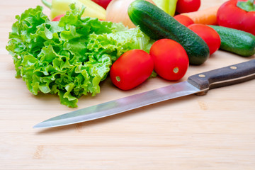 Fresh vegetables and knife on kitchen wooden table.