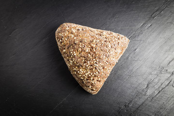 Integral bread in the form of a triangle with linseed, oats and sesame seeds on a black slate table
