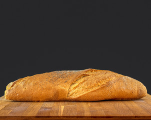 Loaf of bread on wooden breadboard, dark color copy space background