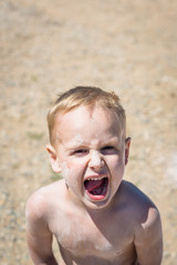 4-year old emotional caucasian child is yelling outdoors in summer day vertical