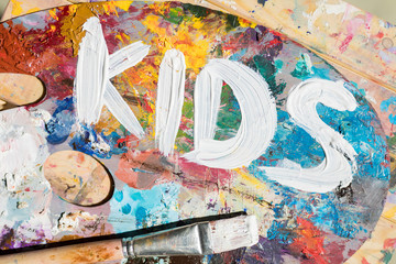 Words kids painted with white gouache on palette of artist with mixture of colors