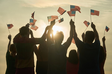 Group of people waving American flags. Silhouette of people with usa flags against evening sunny...