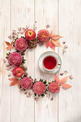 Fruit tea in white cup surrounded by  floral pattern of pink flowers and leaves on white wooden background. Top view, close-up, place for text.