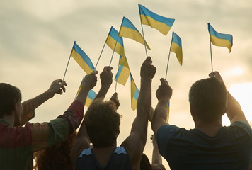 People hold ukrainian flags. Silhouette of patriotic ukrainian crowd, rear view. Gloving evening...