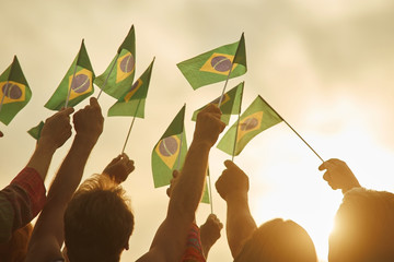 Hands holding brazil flags. Together - we are force, brazilian patriots. Eveining sunny background. - obrazy, fototapety, plakaty