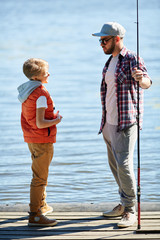 Young man with fishing rod talking to his son while both standing on pontoon © pressmaster